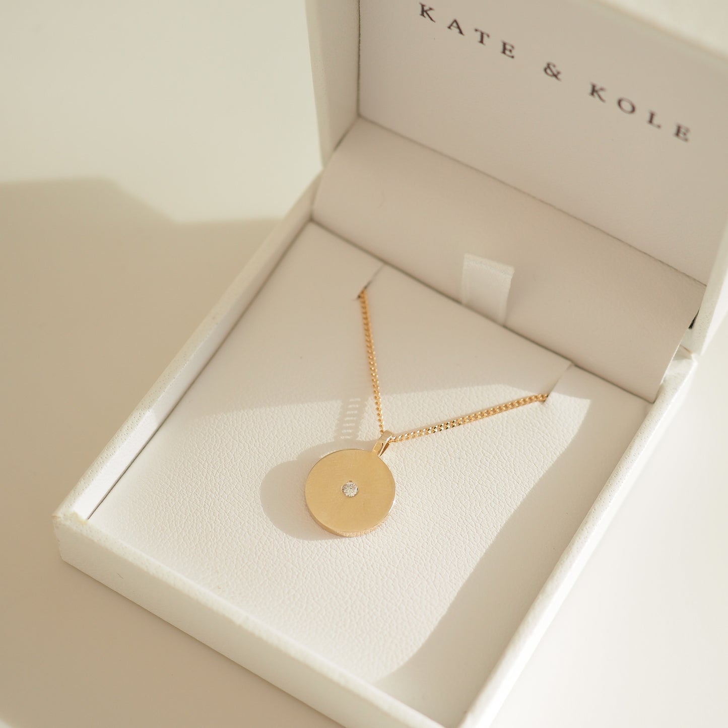 Gold pendant necklace with a small diamond in a white Kate & Kole jewellery box, showcasing luxury design and elegance.