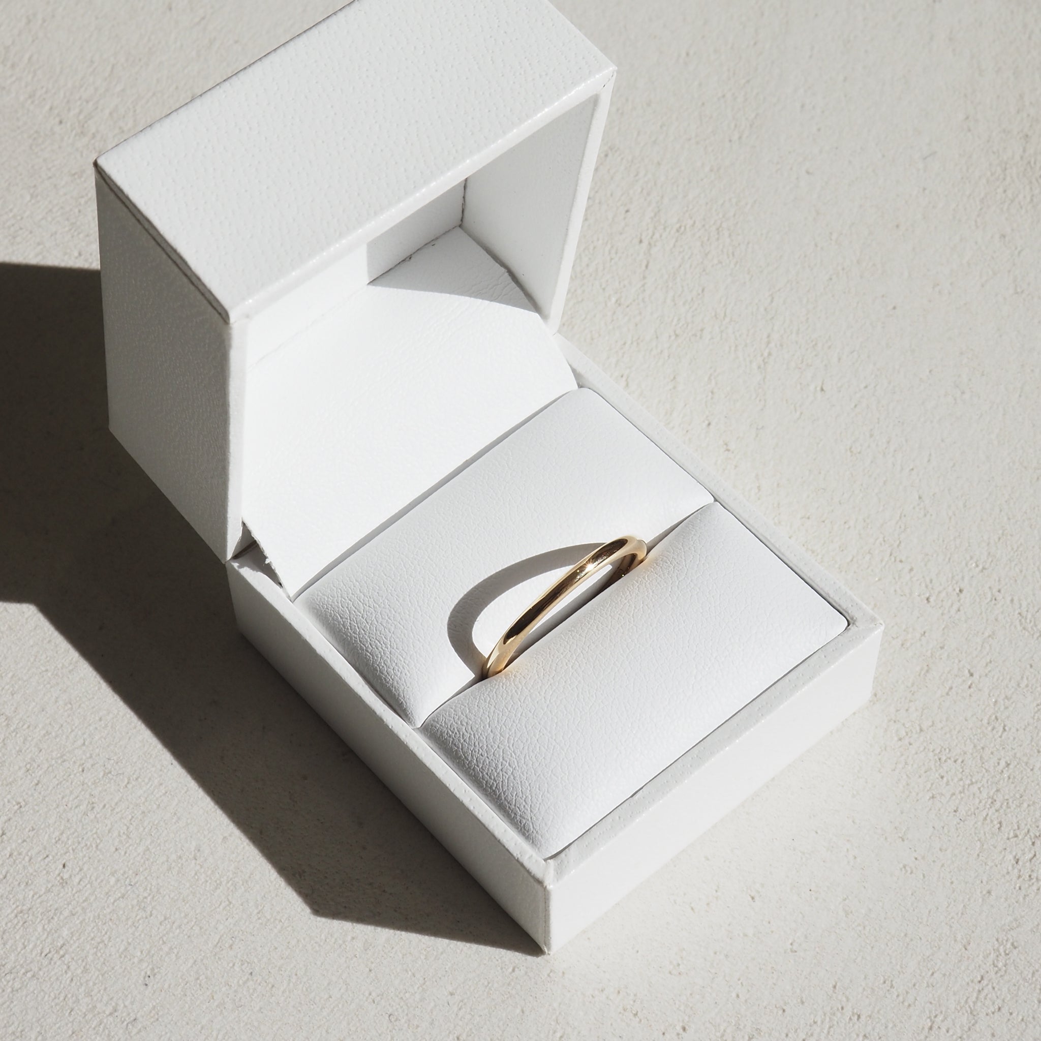 Elegant gold ring in a white leather jewellery box, sunlight casting a shadow, emphasising its luxury and minimalist design.