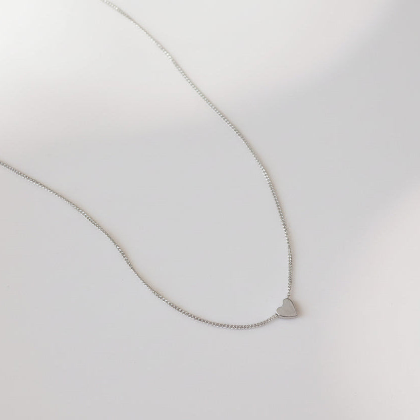 Silver necklace with a small heart pendant on a light gray background
