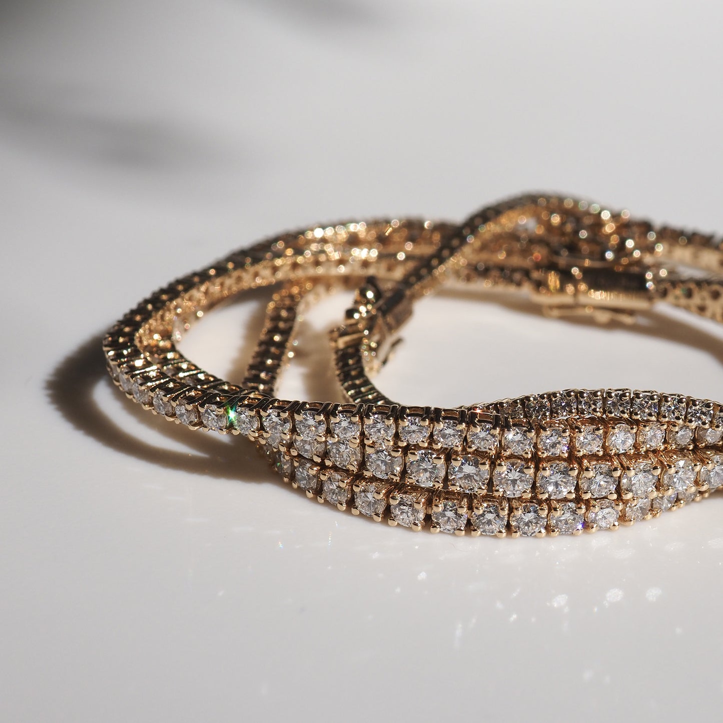 Elegant gold and diamond tennis bracelets on a white surface, glistening in natural light. Perfect for luxury jewellery enthusiasts.