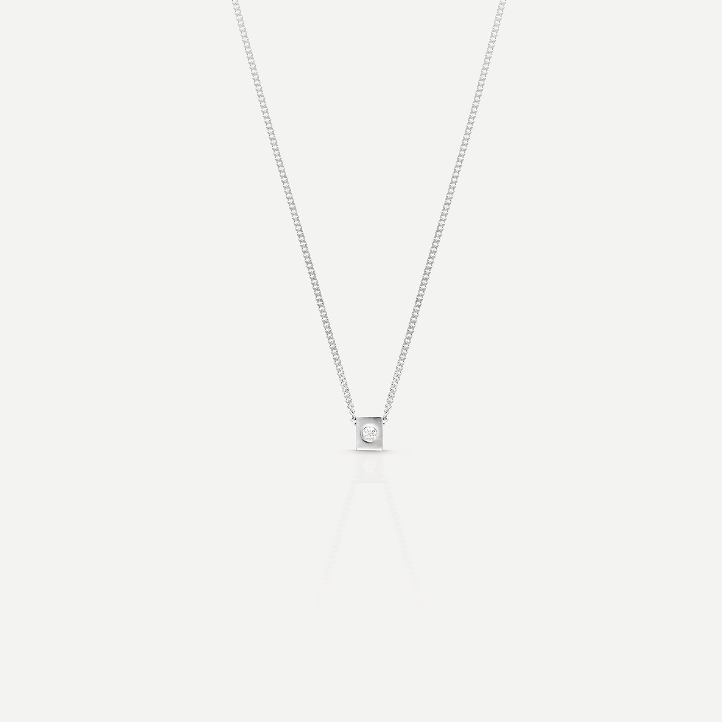 Elegant solitaire diamond pendant on a delicate silver chain, set against a light background, showcasing luxury and sophistication.