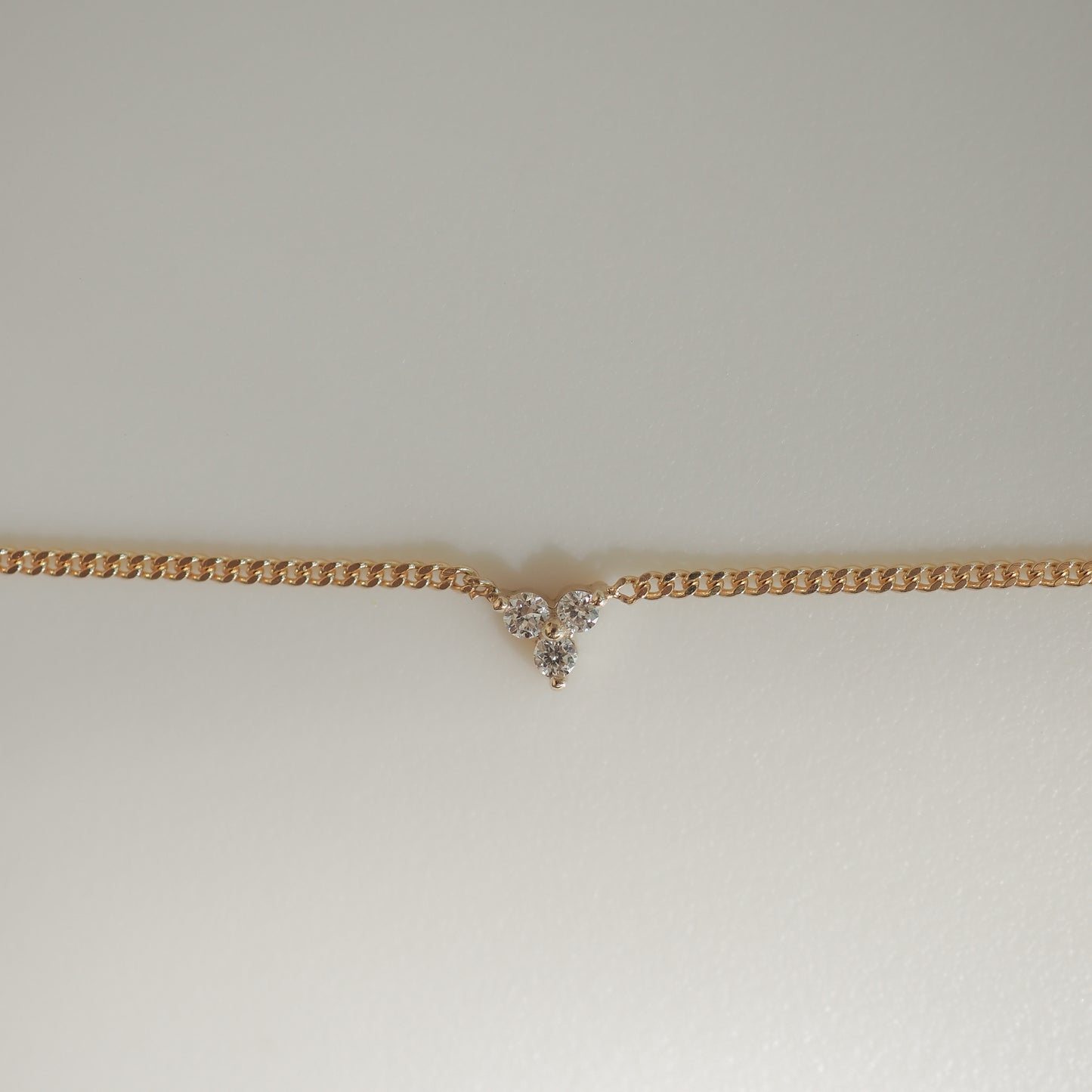 Gold chain necklace with a V-shaped cluster of sparkling diamonds at the centre, set against a soft, light background.