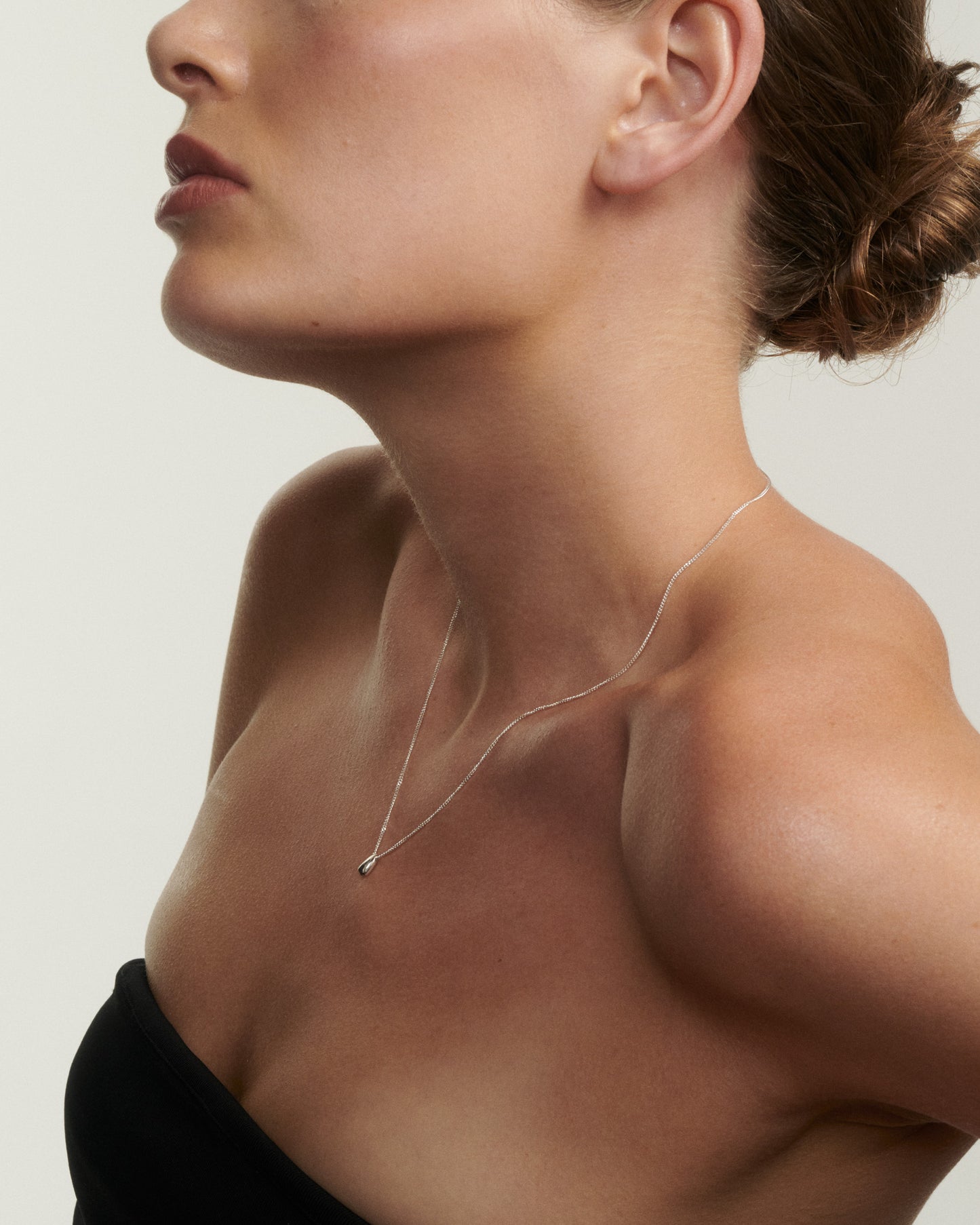 Close-up of a woman wearing a delicate necklace against a neutral background