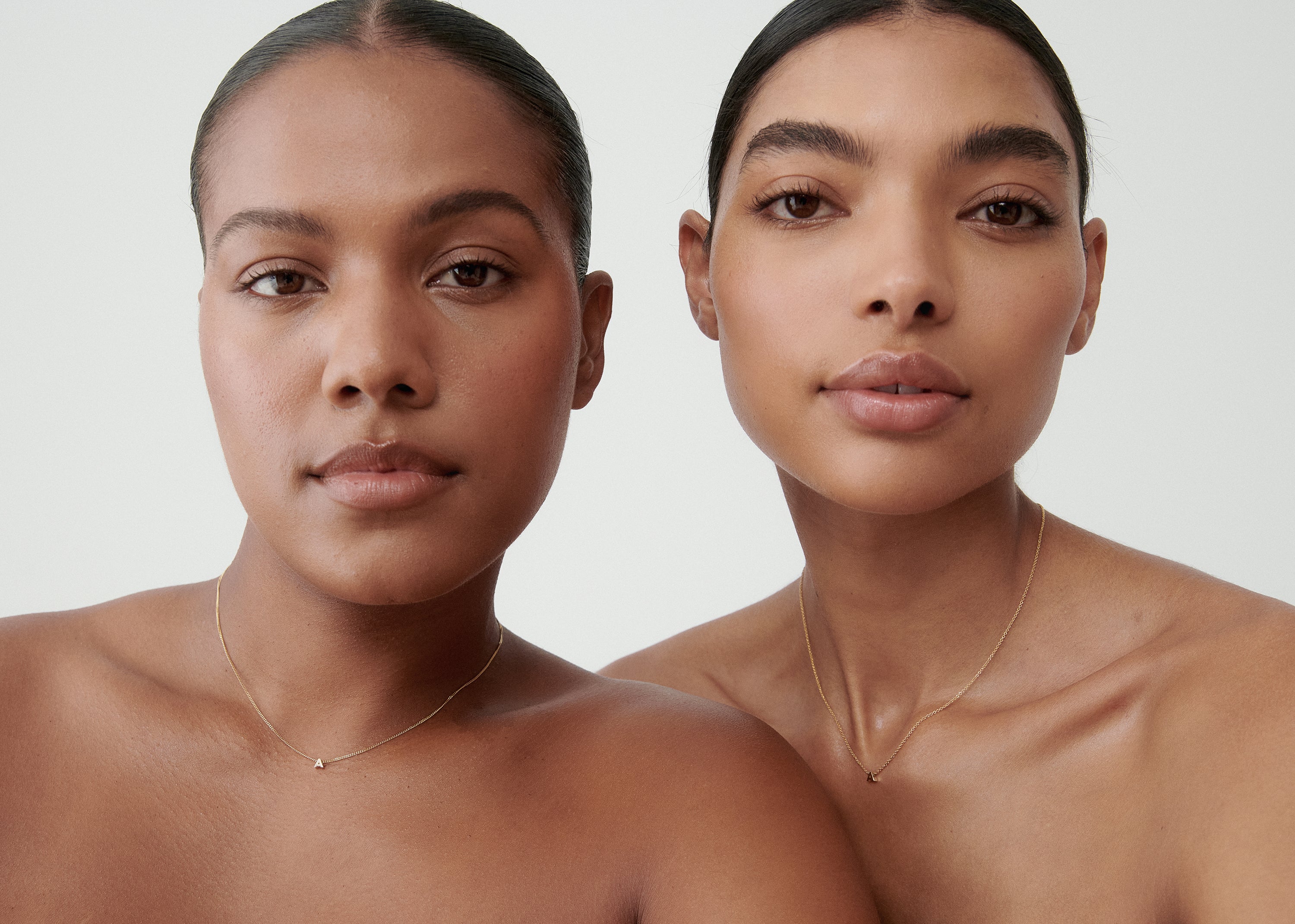 Two women with sleek hair wear minimalist gold necklaces, showcasing luxury jewellery. The focus is on elegance and simplicity.