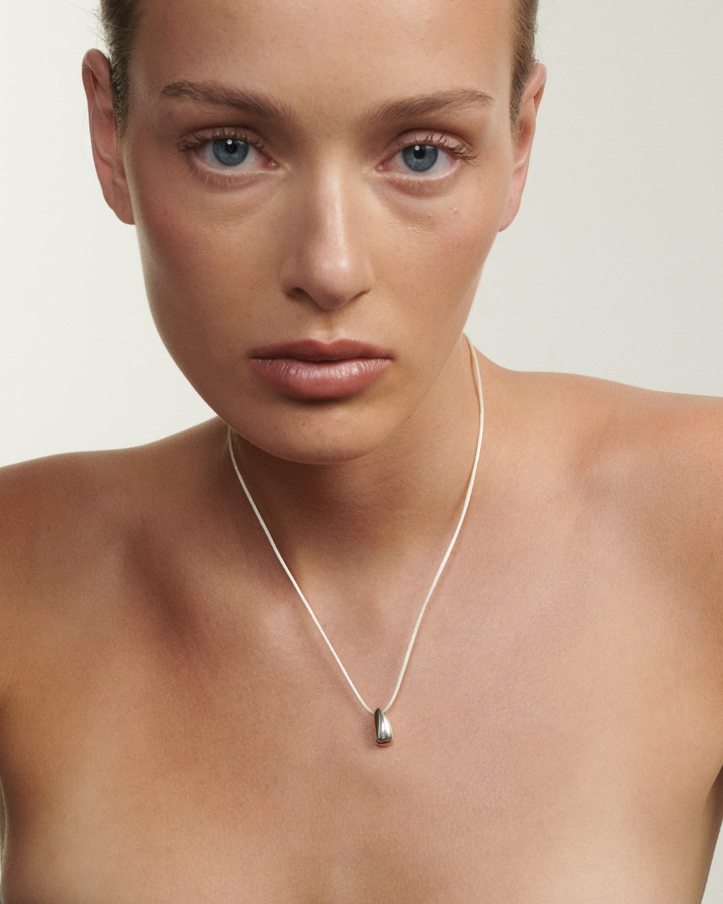 Close-up of a person wearing a silver necklace with a small pendant on a neutral background