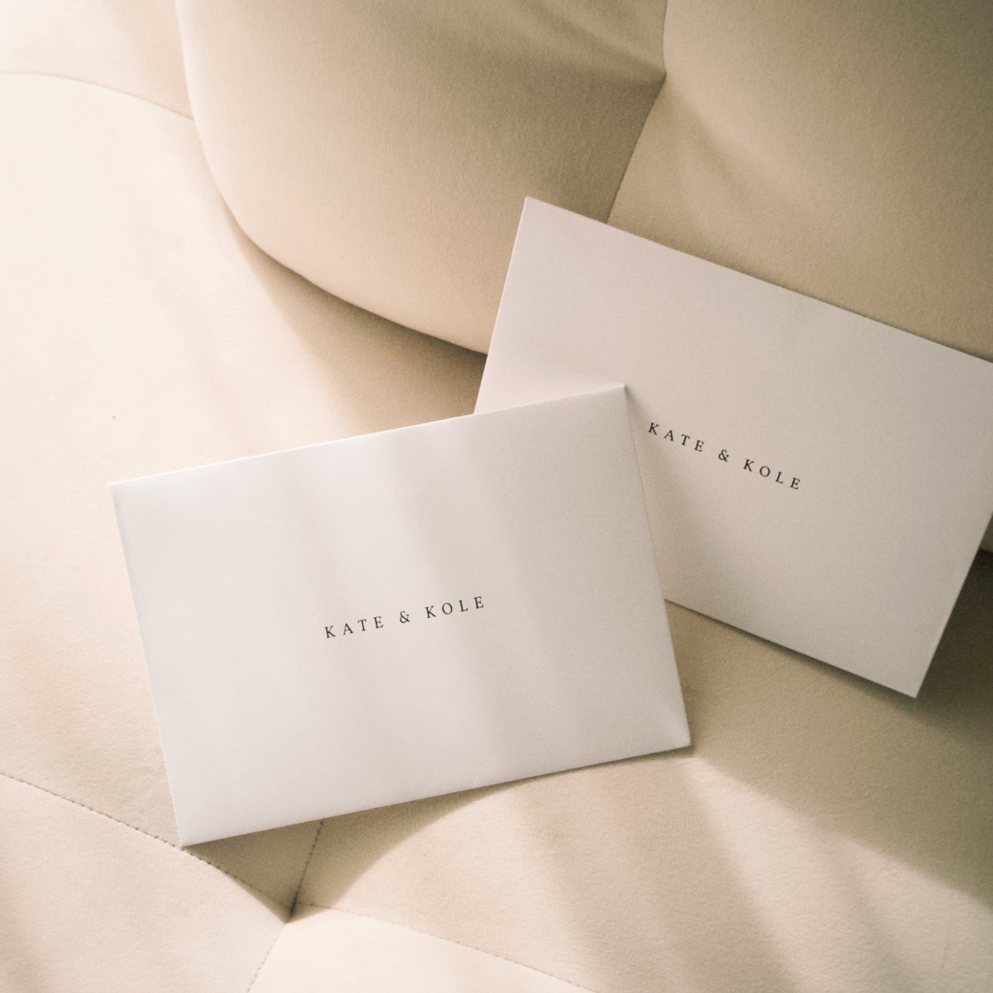 Two beige envelopes with 'KATE & KOLE' branding on a soft beige background