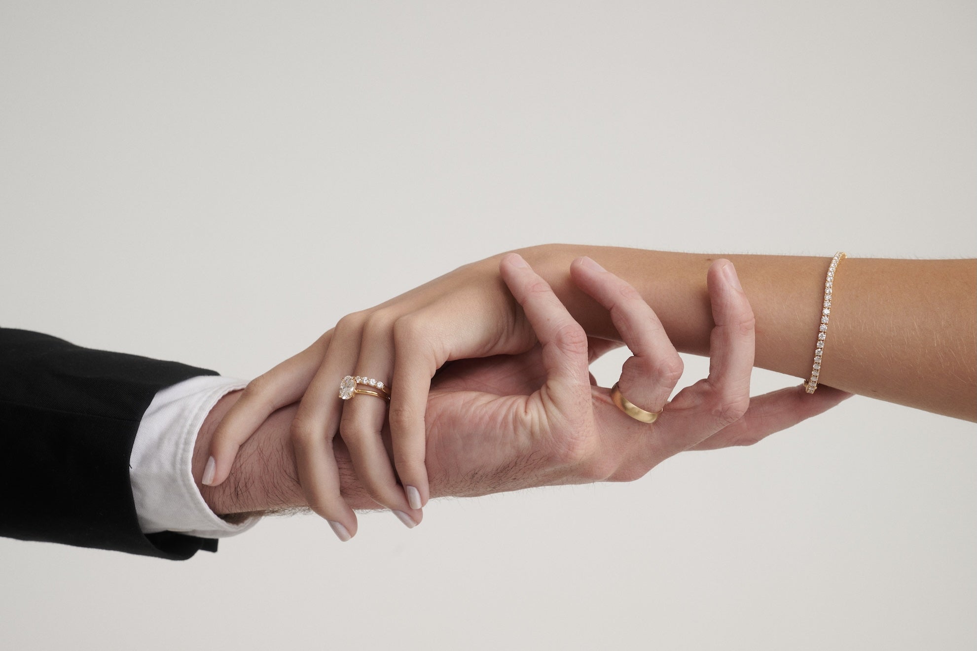 Two hands, one from a person in formal attire and the other from a person in casual wear, holding each other against a plain background.