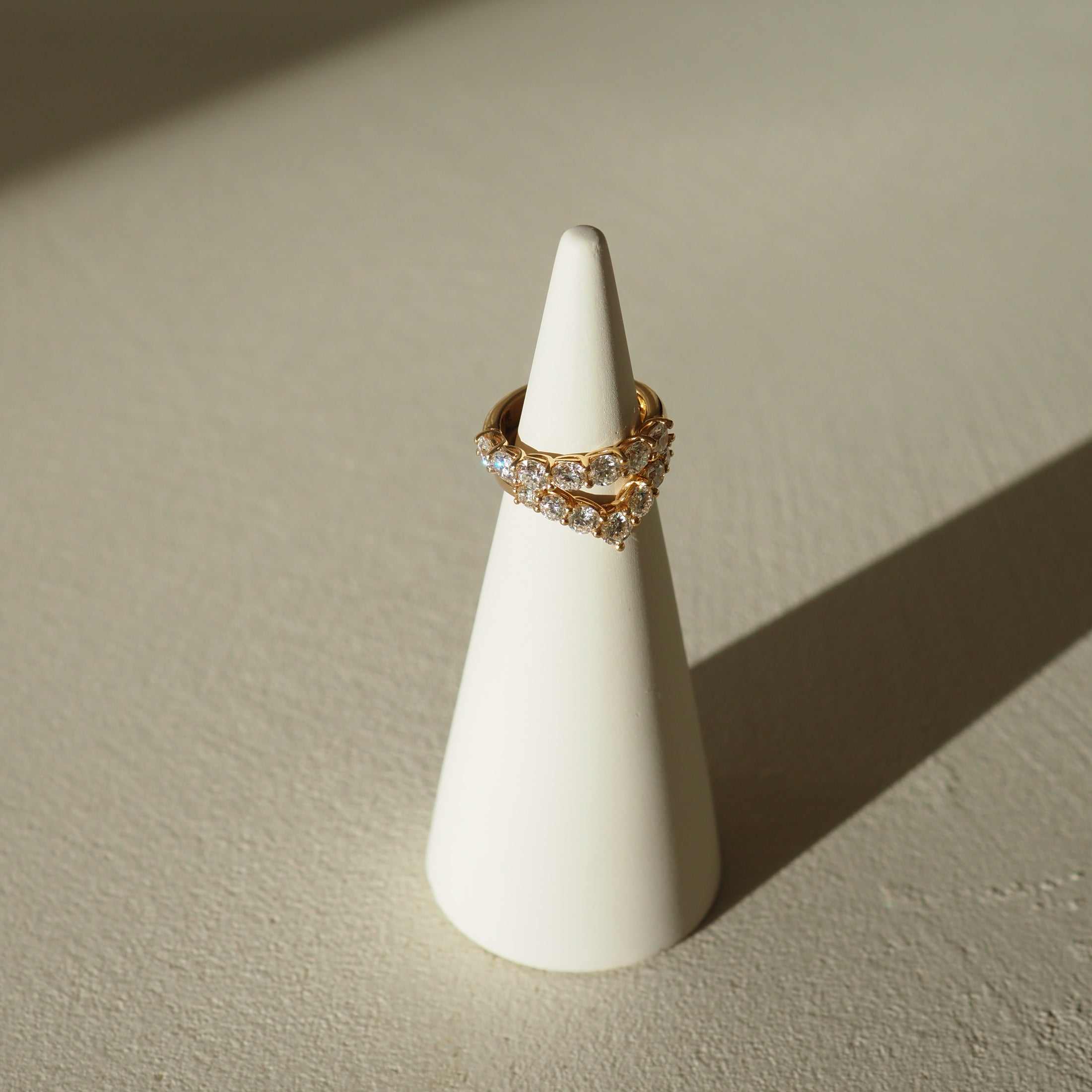 Gold ring with gemstones on a white cone-shaped stand against a beige background