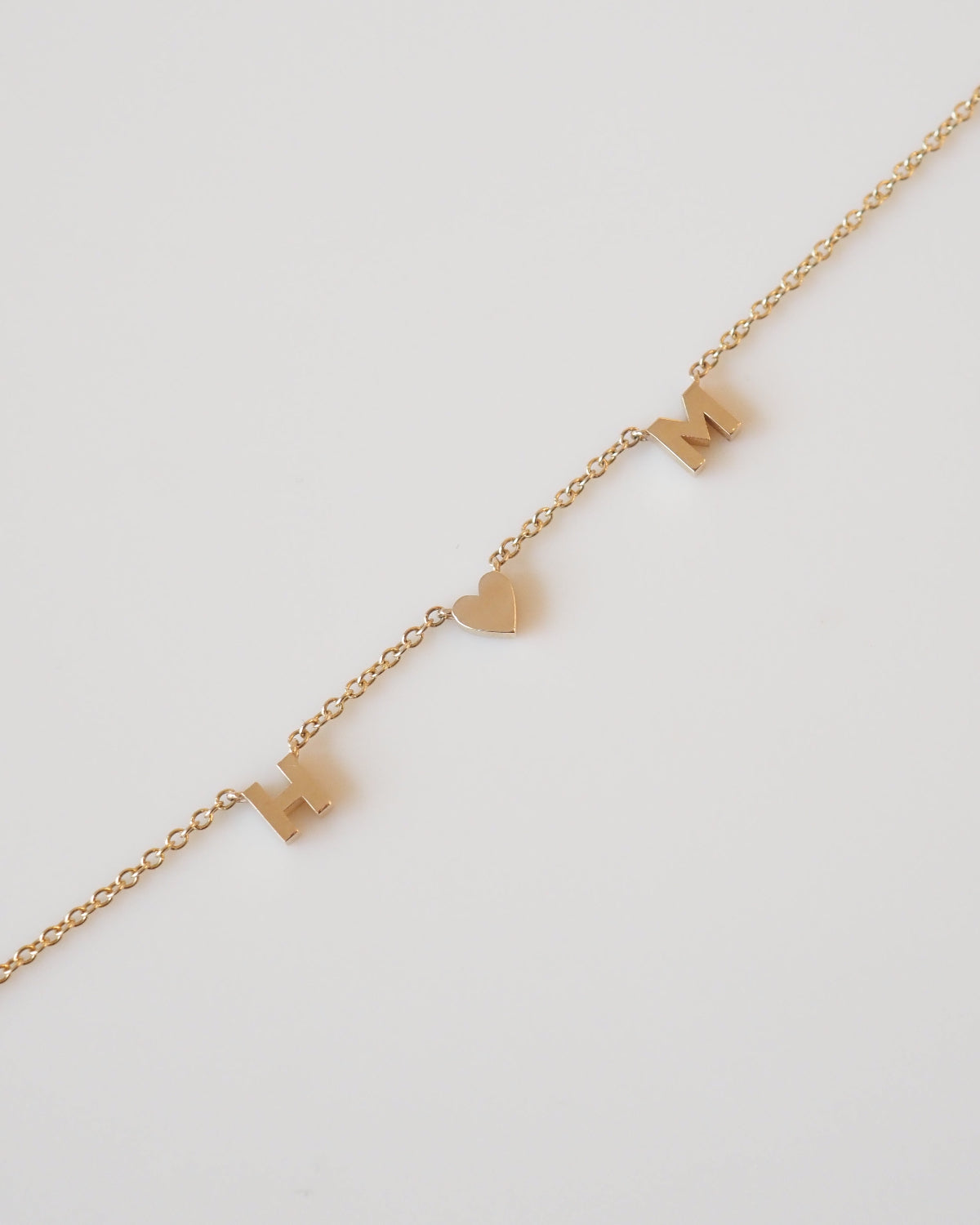 Gold necklace with heart and bow pendants on a light gray background