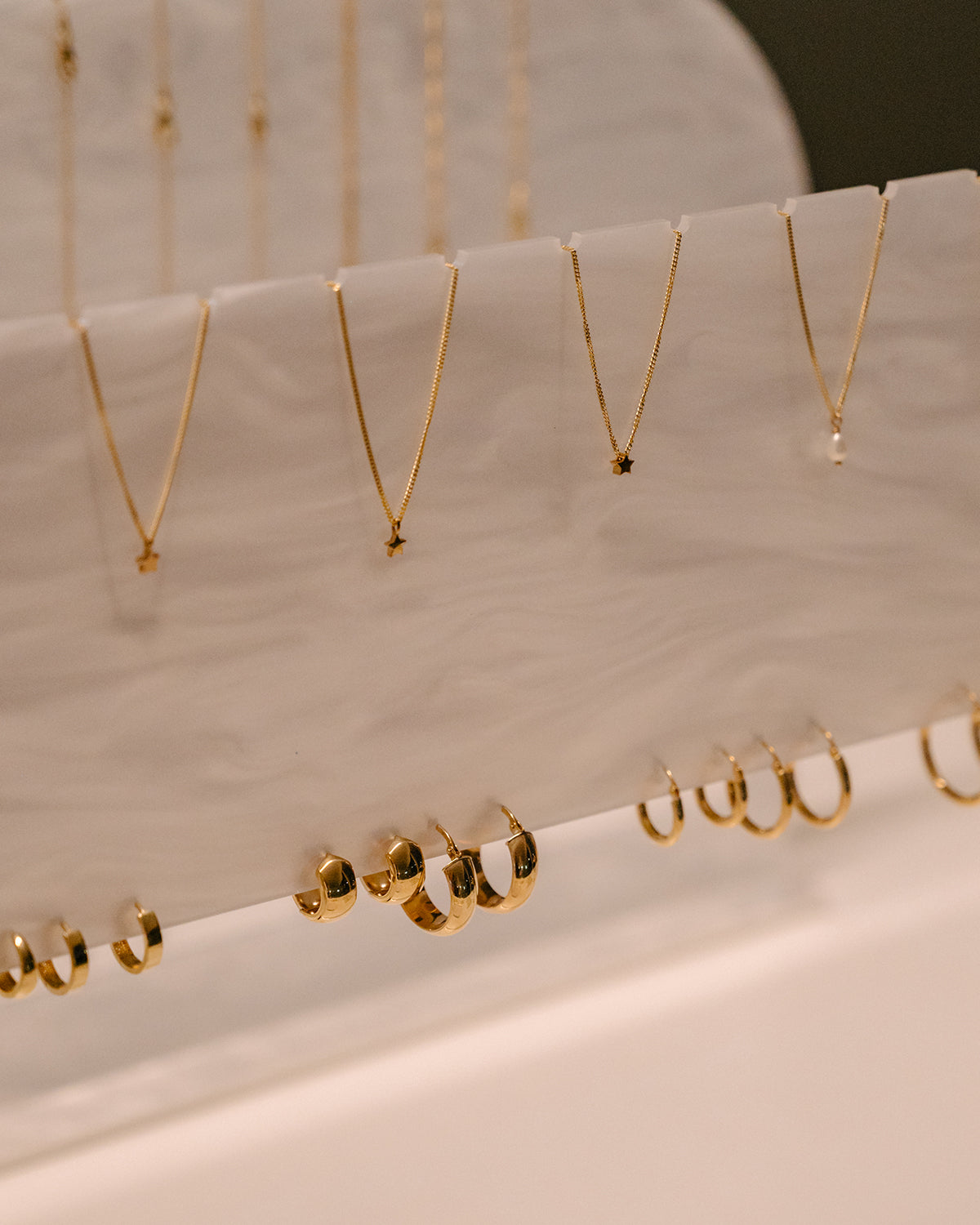 Elegant display of gold jewellery featuring delicate necklaces with star pendants and polished hoop earrings on a marble stand.