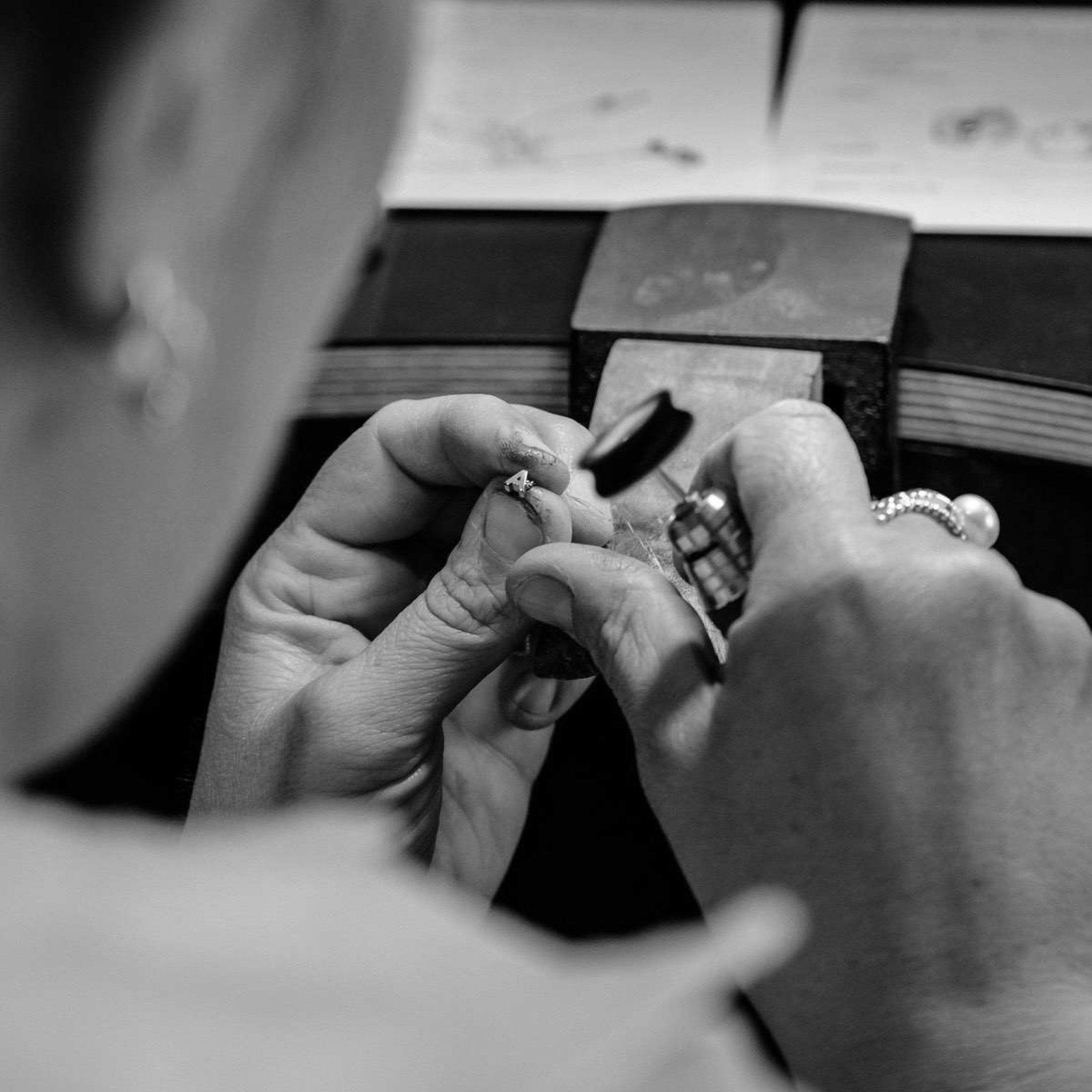 Jeweller crafting a ring with precision tools at a workbench, showcasing high-end luxury jewellery craftsmanship. Black and white image.