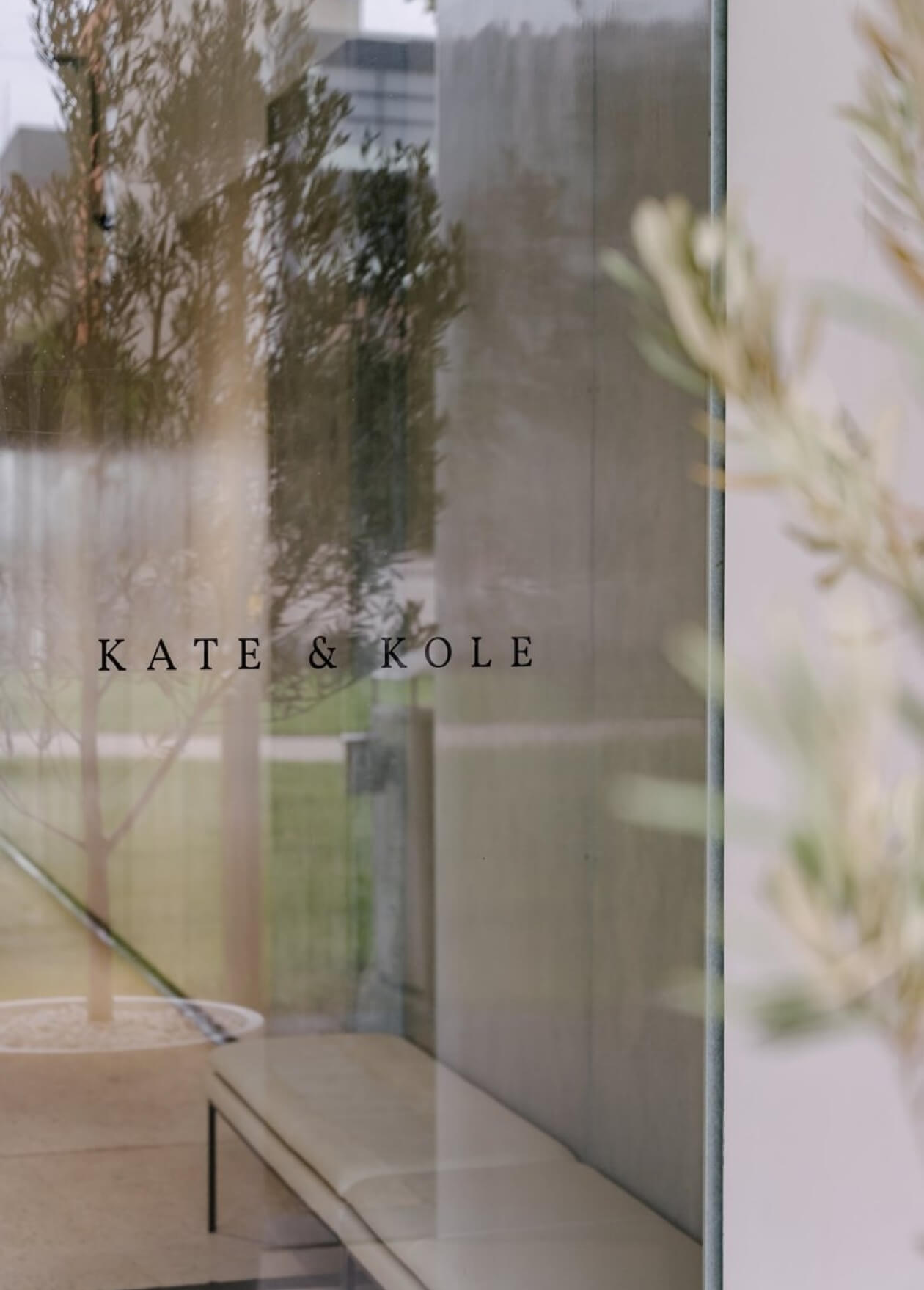 Glass storefront with "Kate & Kole" text, minimalist interior, and greenery reflecting on the window, suggesting luxury jewellery.