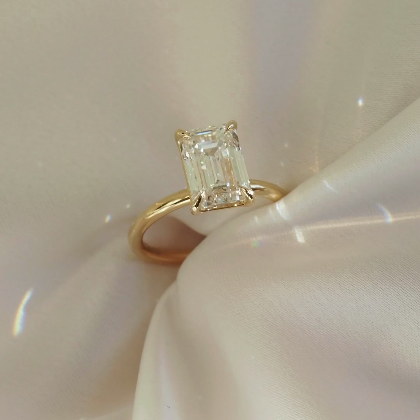 Emerald cut diamond ring with a gold band on a soft, shimmering fabric background. Luxurious, elegant jewellery design.