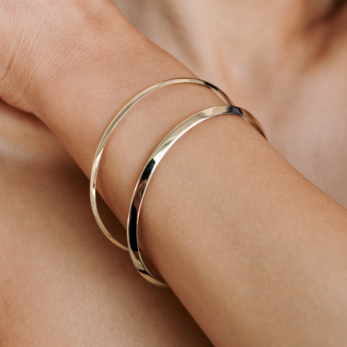 Close-up of a woman's arm wearing two sleek gold bangles, showcasing minimalist luxury jewellery style on smooth skin.