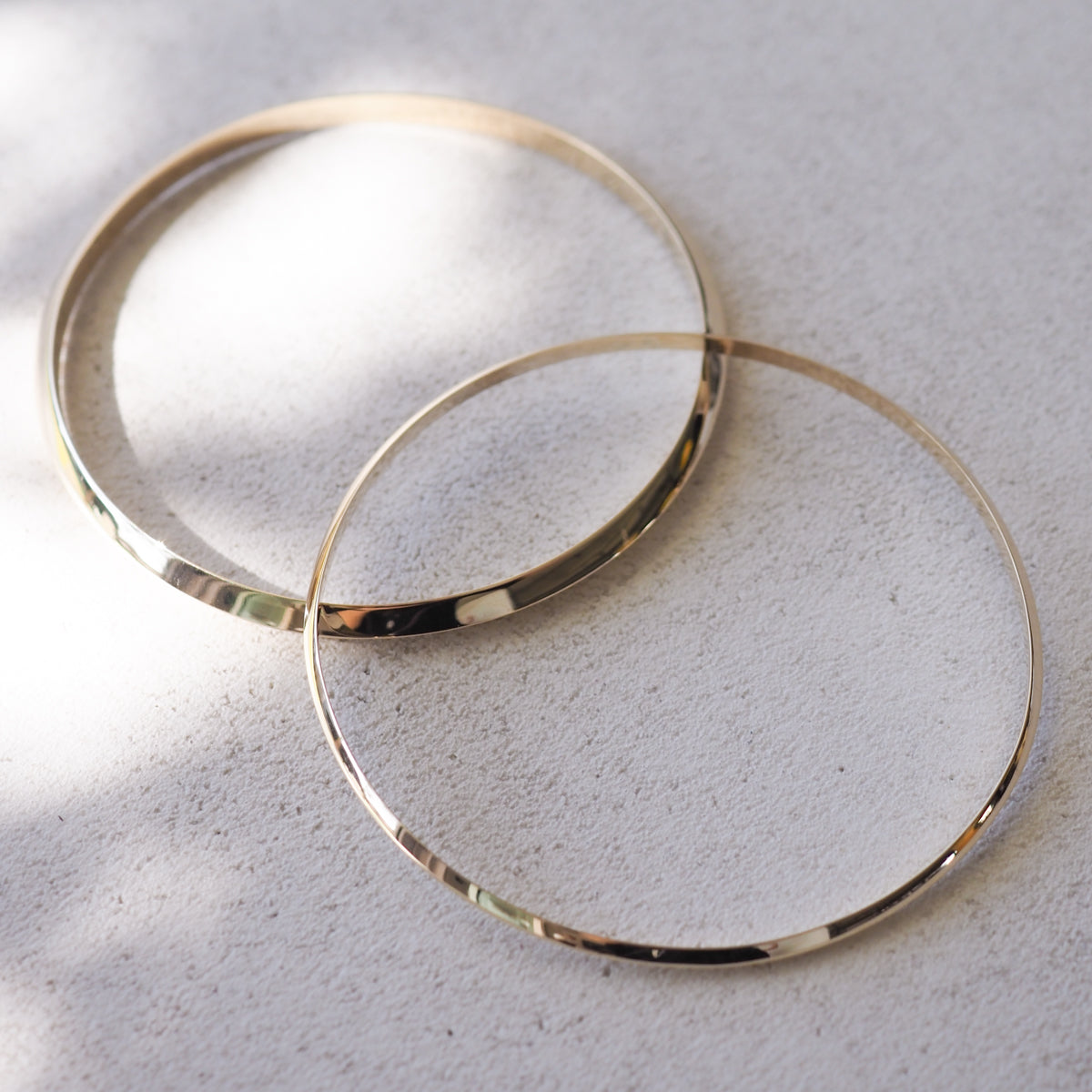 Two sleek gold bangles resting on a textured surface, with soft sunlight casting gentle shadows, exuding elegance and luxury.