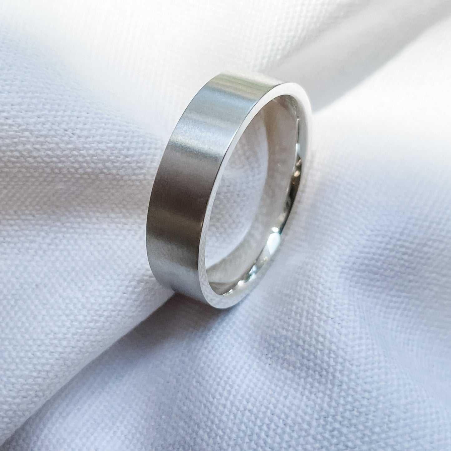 Sleek silver band ring on white fabric, showcasing minimalist luxury jewellery design.